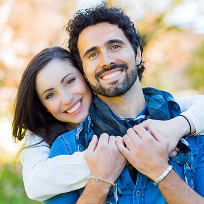 A man and woman embracing each other outdoors with smiles on their faces.