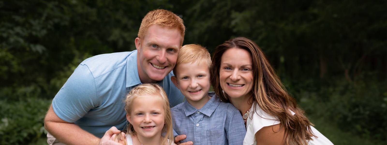 A family photo with a man, woman, and three children posing together outdoors.