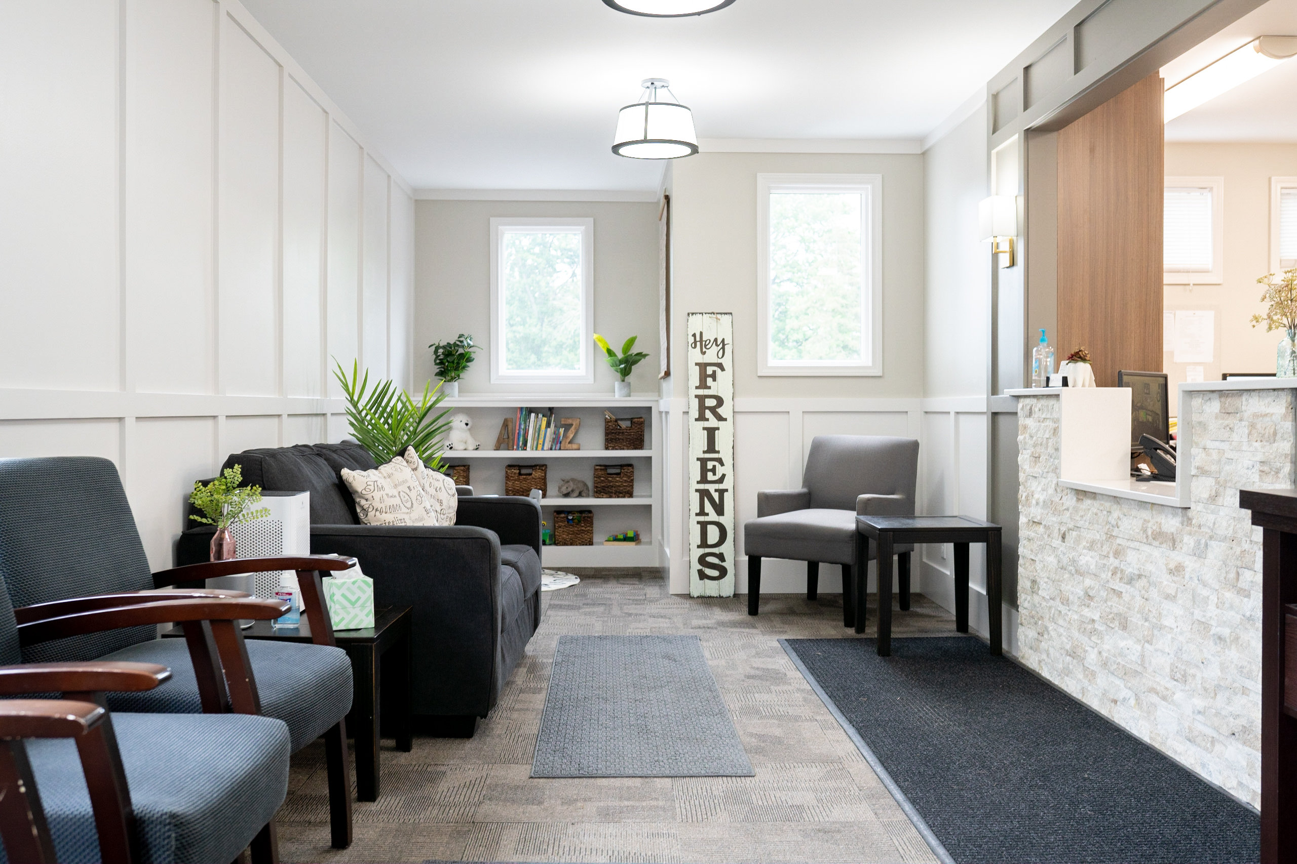 The image shows a modern interior of a waiting area with a clean and organized design, featuring seating, a reception desk, a sign, and a decorative wall.