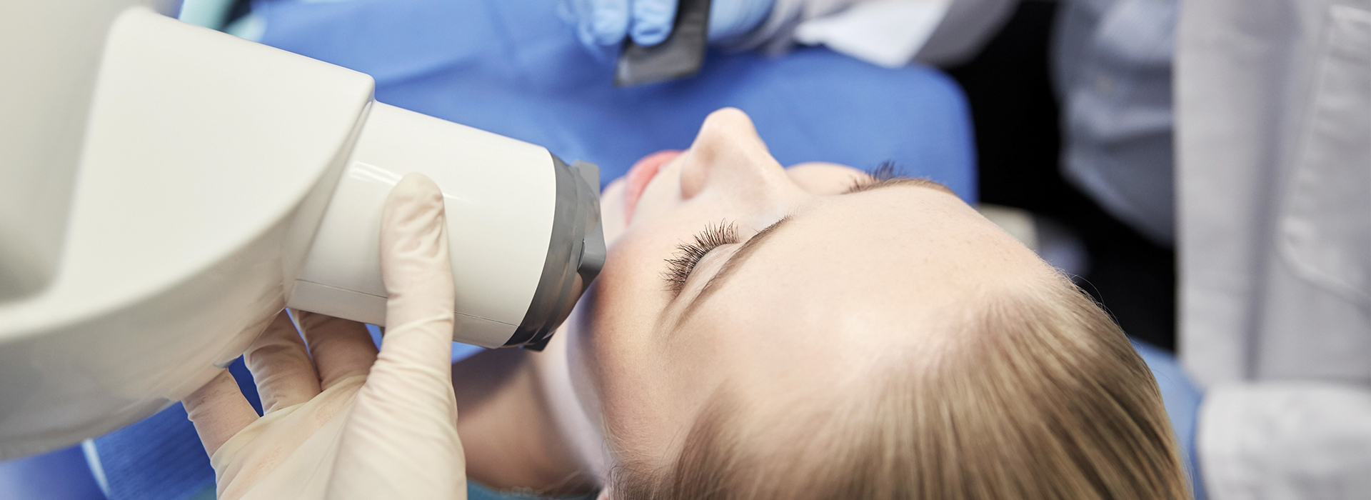 A person receiving a medical treatment with a device attached to their face, surrounded by medical professionals in a clinical setting.