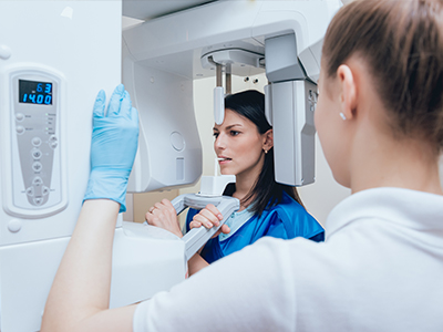 A woman in a blue jacket stands next to a large medical imaging machine with a digital display, while another person looks at the screen.