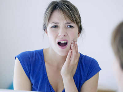 The image shows a woman with her mouth open, expressing surprise or shock, with her hand on her face near her mouth, set against a blurred background.