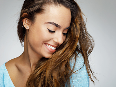 The image features a woman with long hair smiling at the camera  she s wearing a blue top and has her hair pulled back.