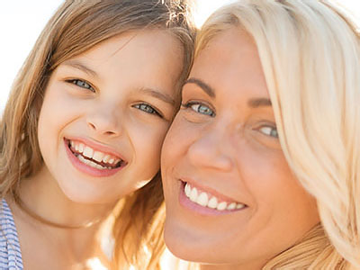 A woman and a young girl pose together with smiles, capturing a joyful family moment.