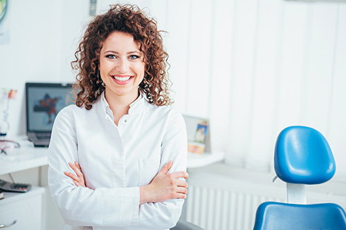 The image shows a woman with curly hair standing in an office setting, smiling at the camera.
