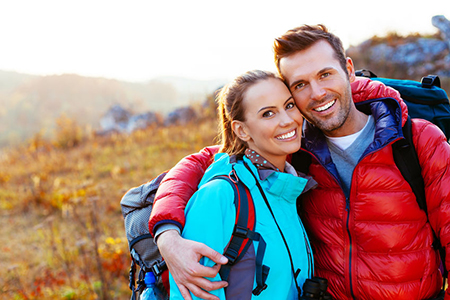 Man and woman posing with backpacks in outdoor setting, smiling at camera.