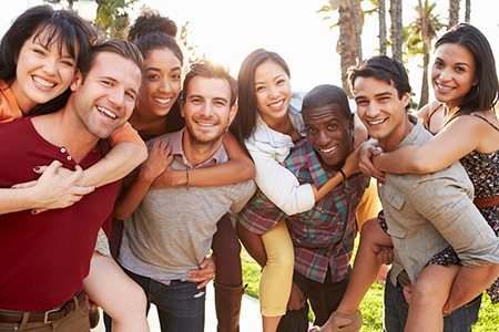 The image shows a group of people standing close together outdoors during the day with smiles on their faces, posing for a photo.
