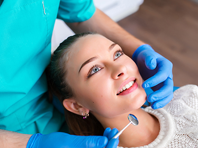 A young woman receiving dental care with a smiling expression while seated in a dental chair, with a dentist performing the procedure.