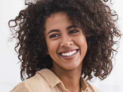 A woman with curly hair smiles at the camera, wearing a light-colored top.